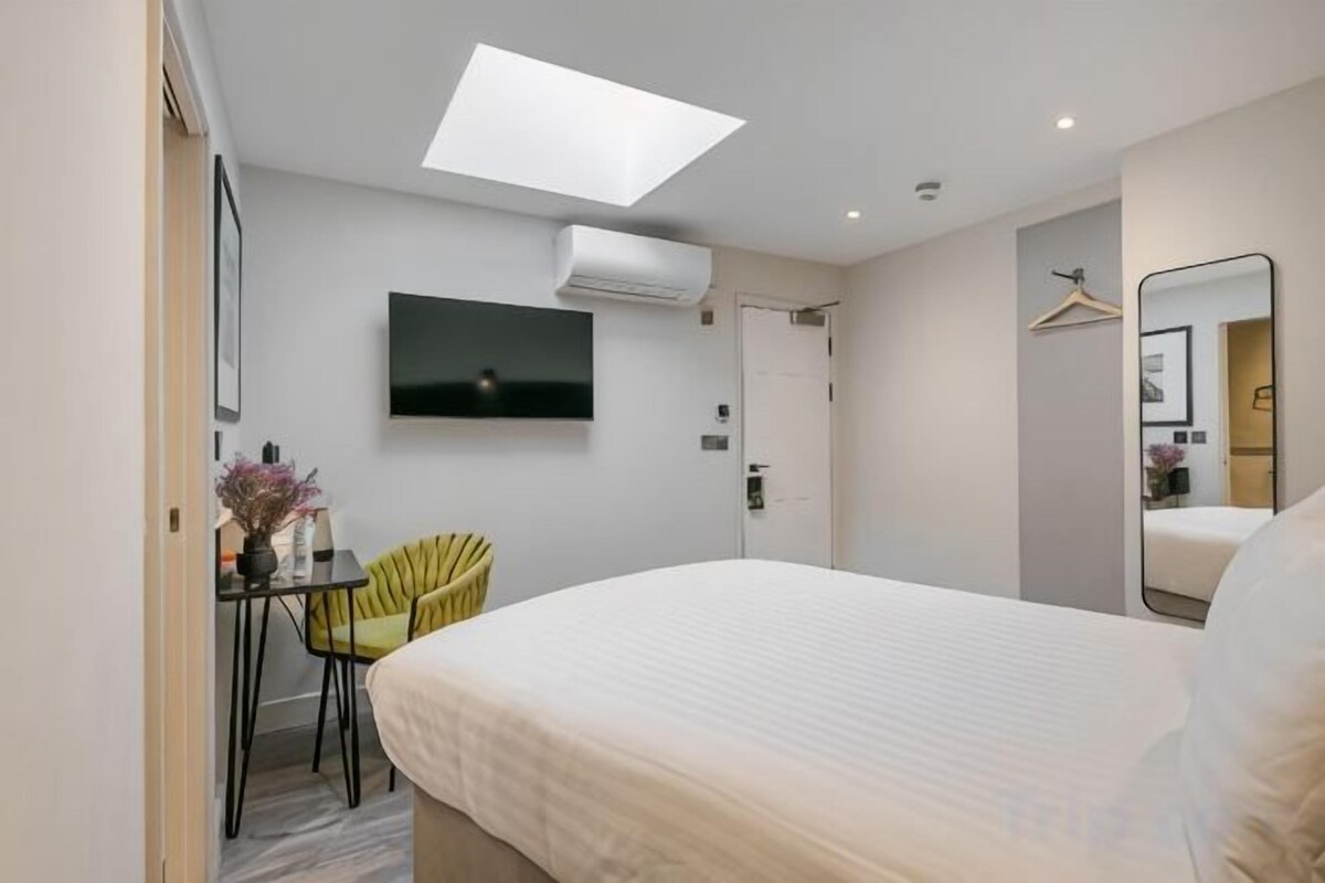 A hotel room with a bed, a desk, a chair, a TV, and a mirror.