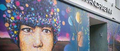 A building with a colorful mural on the exterior wall, a sign reading "ST. PANCRAS INN," and a door with a keypad lock.