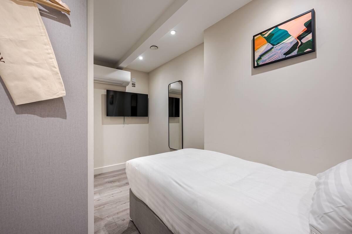 A modern hotel room with a bed, a mirror, and a painting on the wall.
