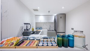 Una cocina moderna con paredes de mármol, horno empotrado y refrigerador. Hay varios alimentos y bebidas en la encimera.