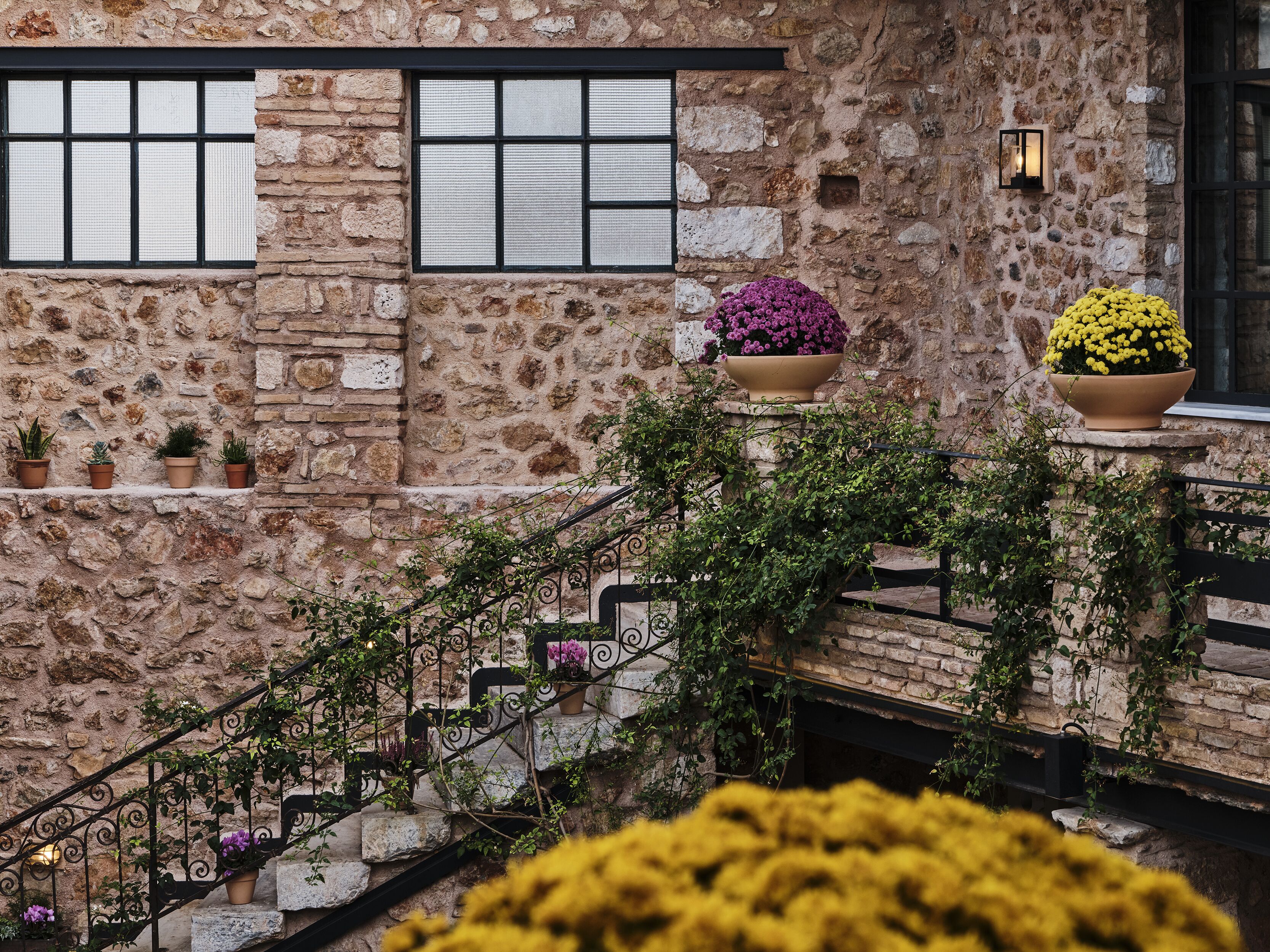 A stone building with a staircase, potted plants, and a window with a black frame.