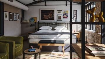 Une chambre à coucher moderne avec un grand lit, un fauteuil vert, une petite table ronde et un tapis coloré.