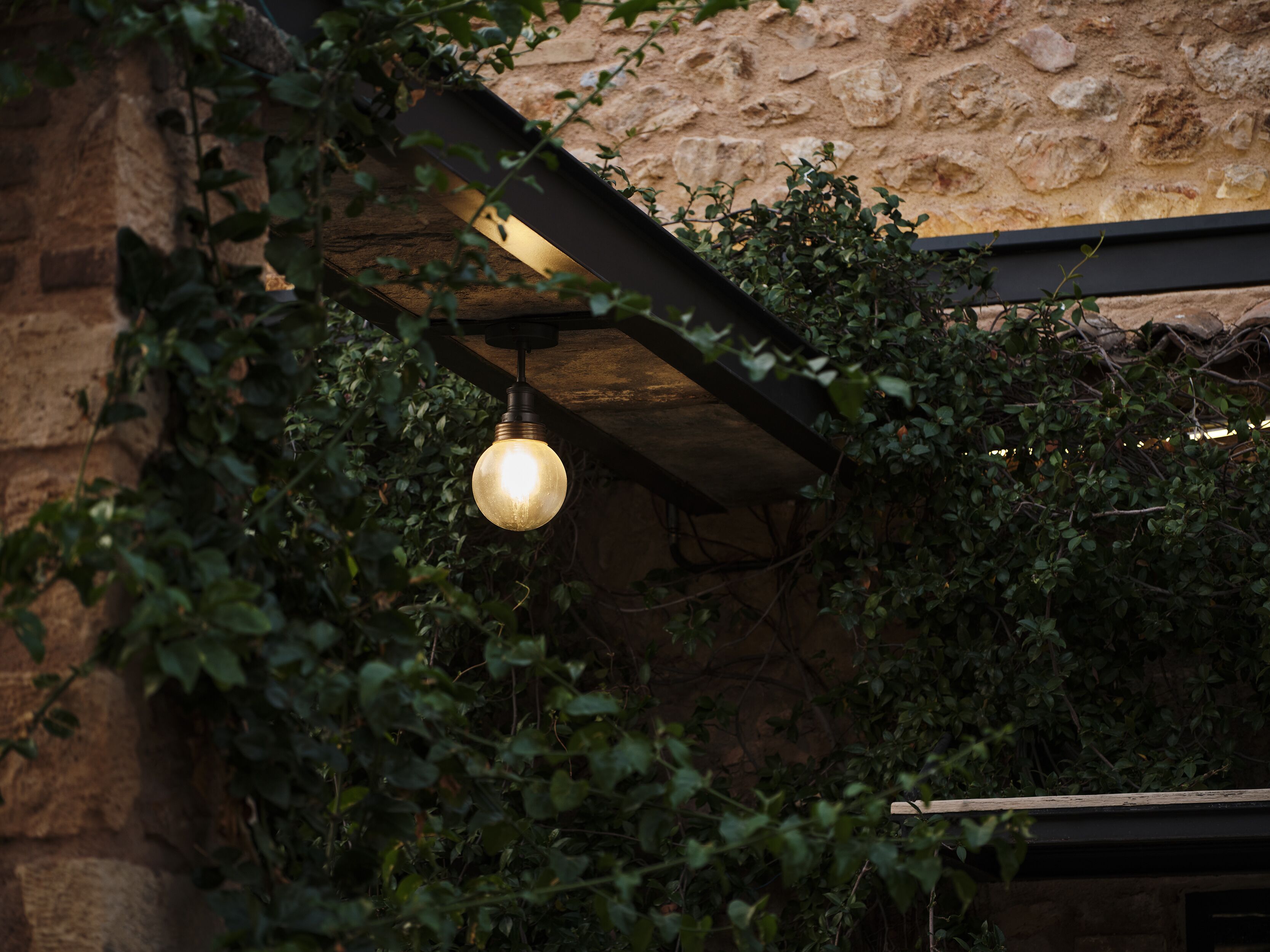 Un luminaire suspendu dans un bâtiment en pierre, entouré de verdure.
