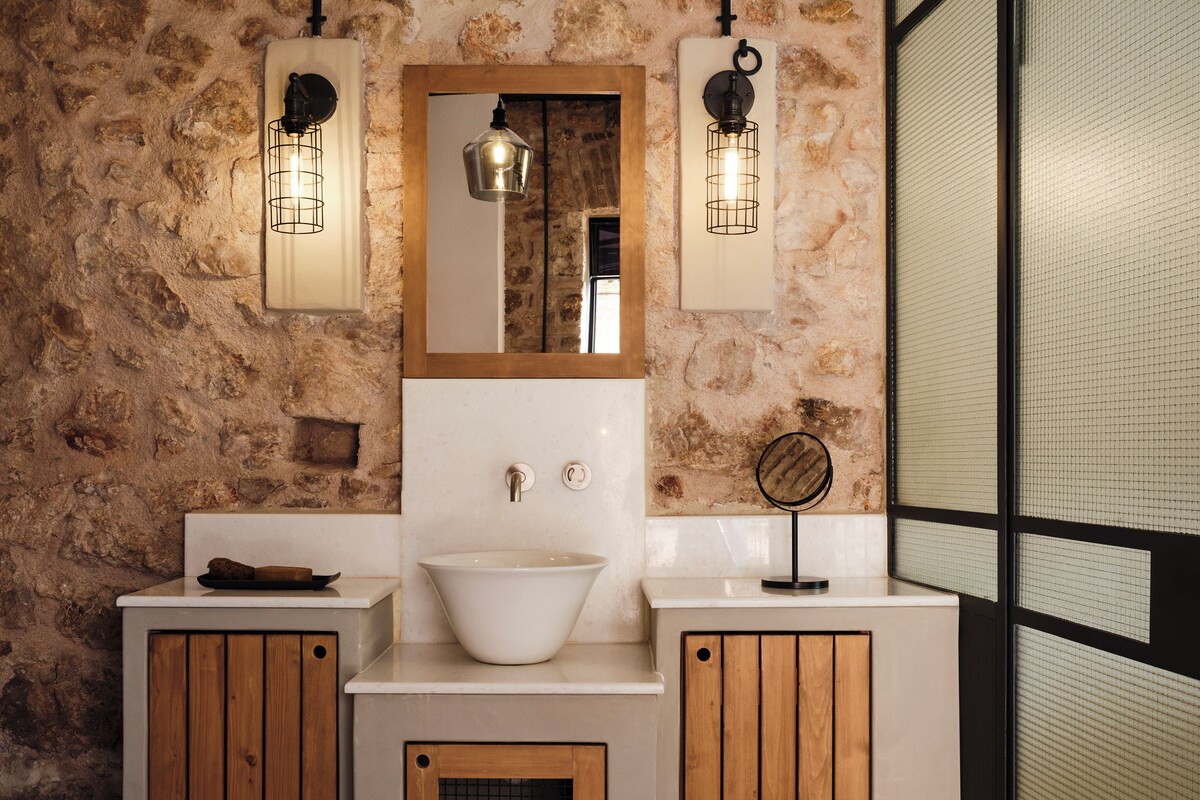 Un baño con pared de piedra, un lavamanos blanco, armarios de madera y dos luces empotradas.