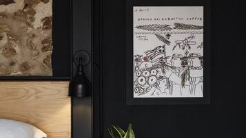 A bedroom with a bed, a nightstand with a plant, a lamp, and a framed picture on the wall.