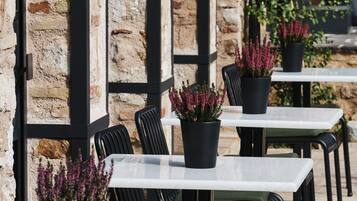 Terrasse mit Tischen, Stühlen und Pflanzen in Töpfen, dazu eine Steinmauer.