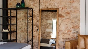 A room with a bed, a sofa, a bookshelf, and a mirror reflecting a window.