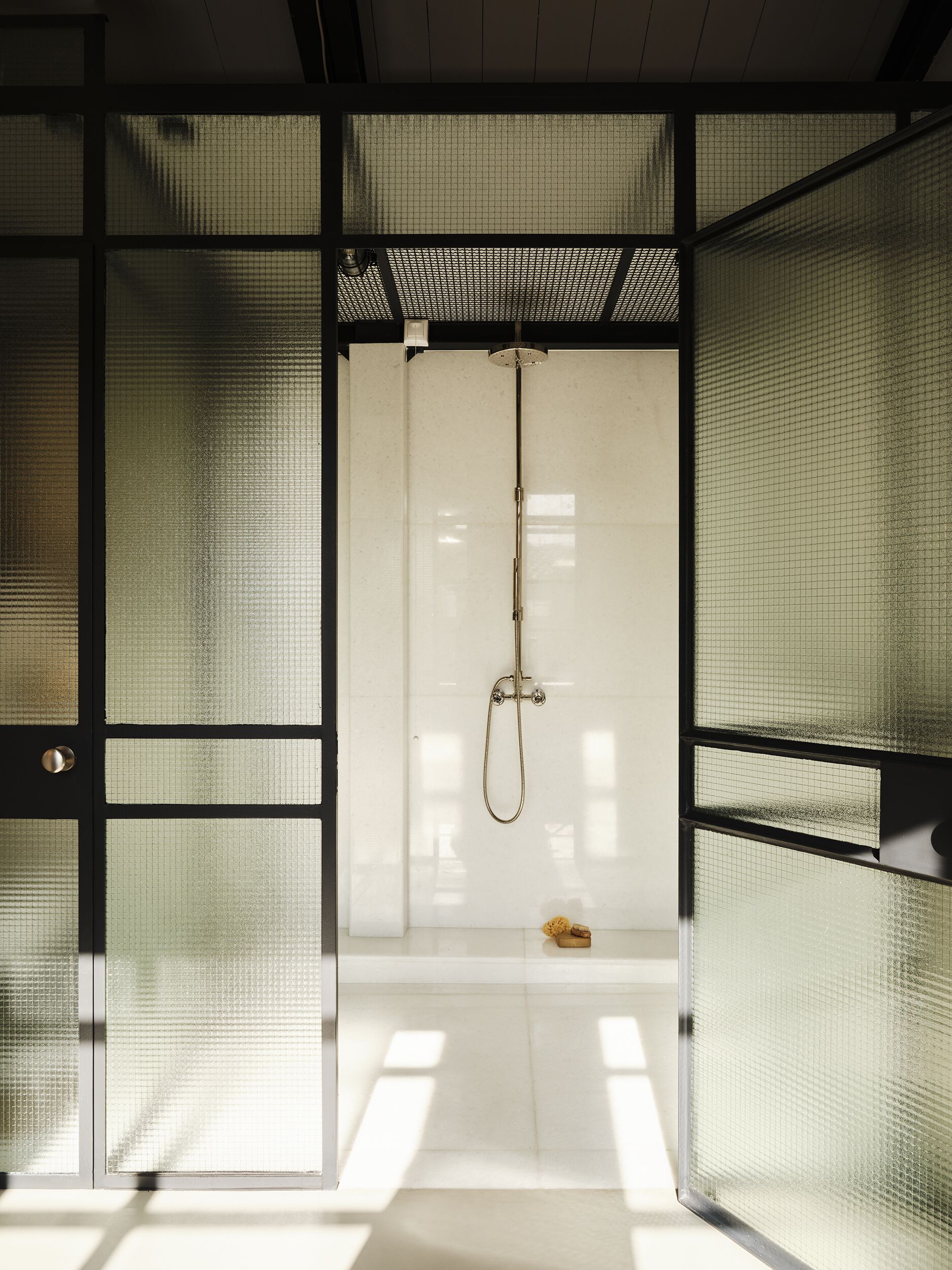 Une pièce de style japonais traditionnel, dotée de portes coulissantes, d’une douche suspendue et d’un petit tabouret en bois.