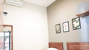 A bedroom with two single beds, a wooden headboard, a wall-mounted air conditioner, and three framed pictures. - Casa TS 16 Guest House by Pesen Kamar (Malang)