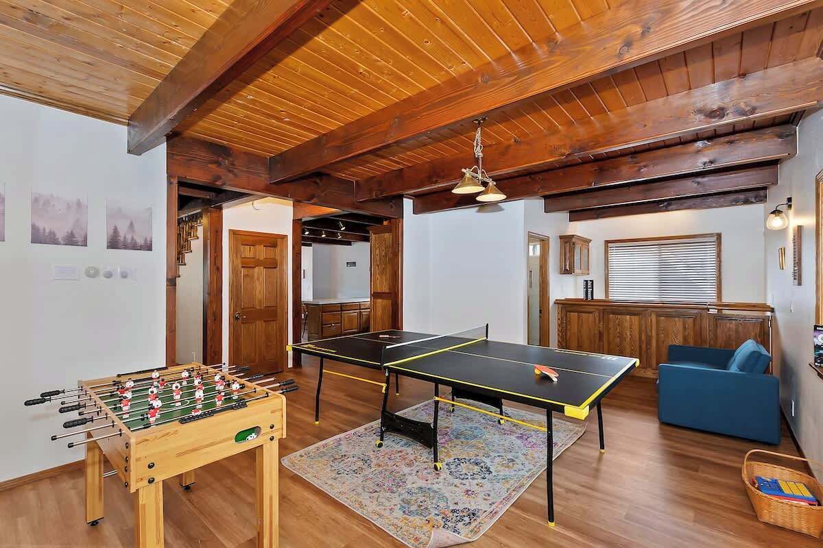 A room with a foosball table, ping pong table, and a sofa.