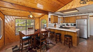 L’intérieur d’un chalet en bois comprend un coin repas, une cuisine et une grande fenêtre donnant sur l’extérieur.