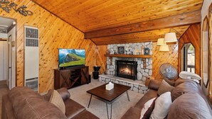 Un salon chaleureux avec une cheminée en pierre, un plafond en bois, un canapé en cuir et un téléviseur.