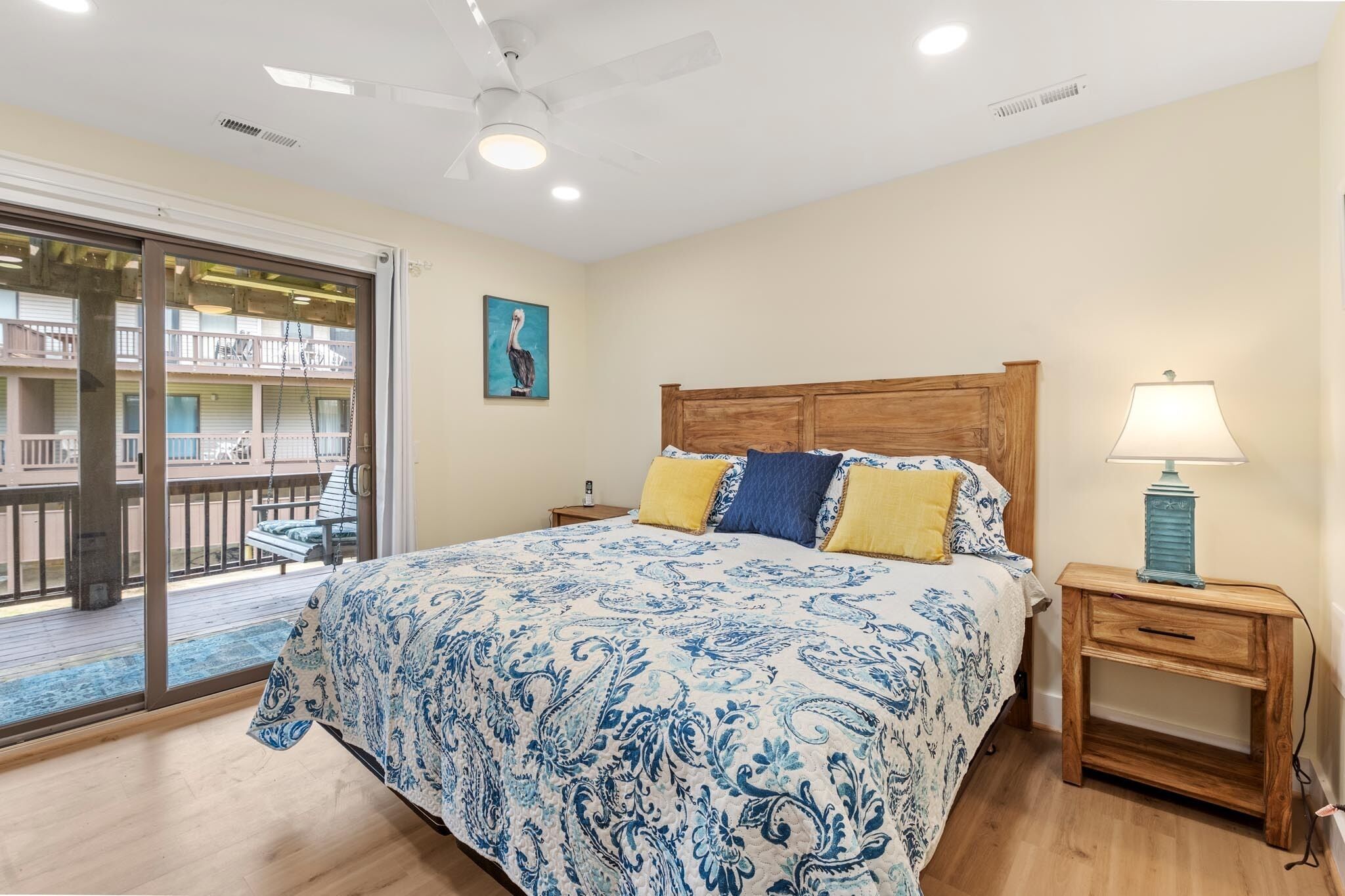 Quarto com cama, mesa de cabeceira, abajur, quadro e varanda com balanço.