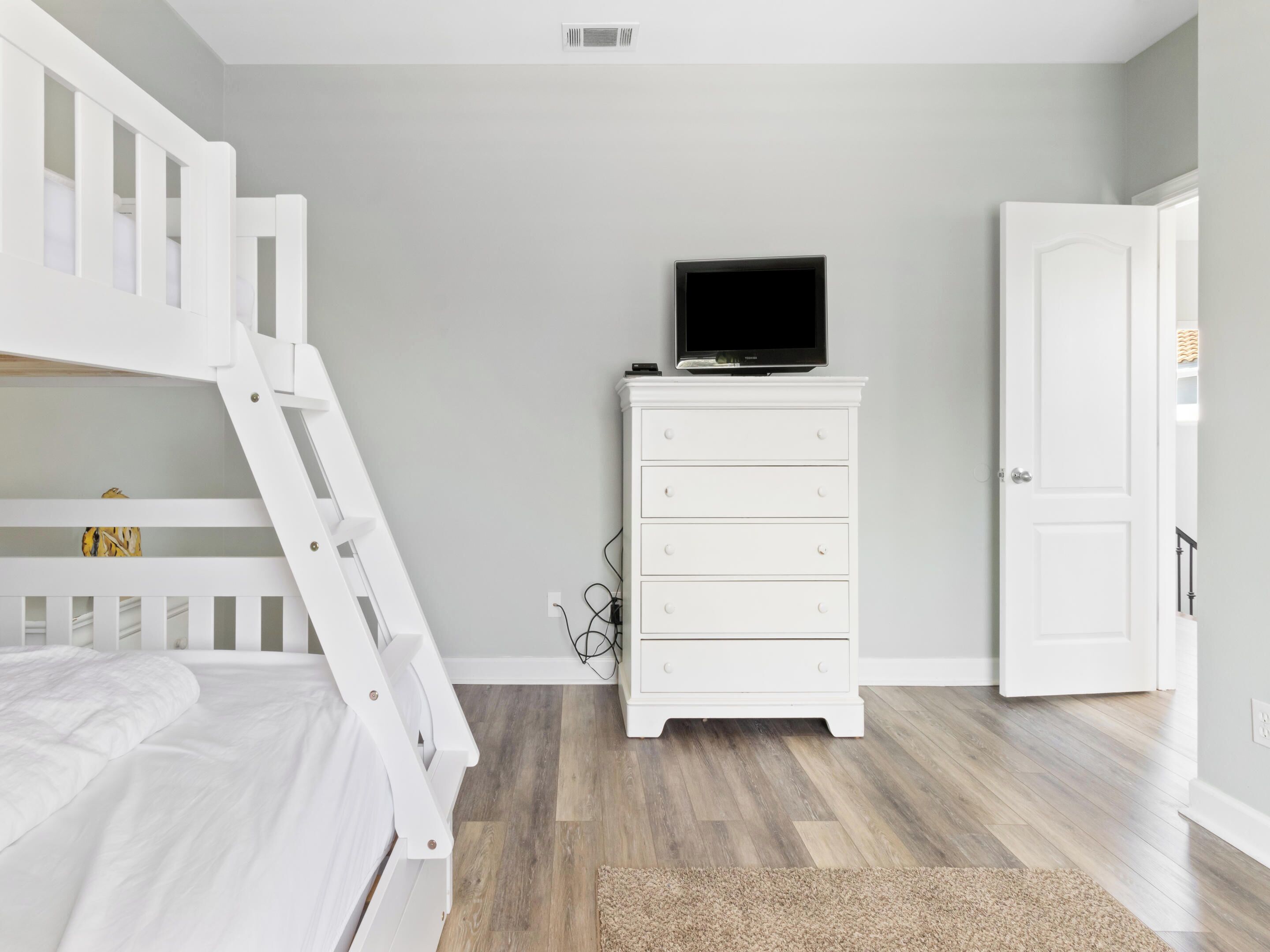 A bedroom with a bunk bed, a white dresser with a television on top, and a door to the right.