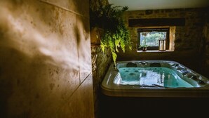 A hot tub in a rustic stone room with a window and plants. - Romantic stay with spa, sauna and home cinema (Beaumontois-en-Périgord)