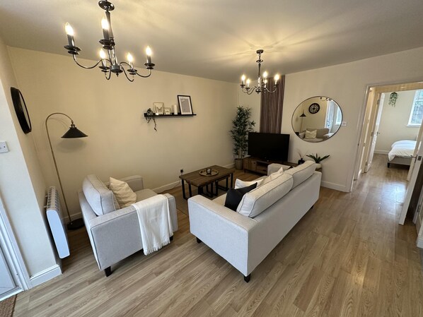A living room with a sofa, a coffee table, a TV, a chandelier, and a mirror.