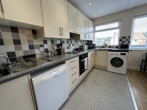 A modern kitchen with white cabinets, a dishwasher, a washing machine, and a window with blinds.