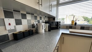 A kitchen with a checkered backsplash, a kettle, a microwave, and a window with blinds. - Charming 2-bed Apartment in Danbury, Essex (Chelmsford)