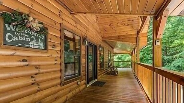 Une cabane en bois dotée d’un porche abrité, d’une pancarte de bienvenue et offrant une vue sur la verdure.