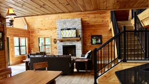 L’intérieur d’un chalet en bois, avec une cheminée, un canapé, une table à manger et un escalier.