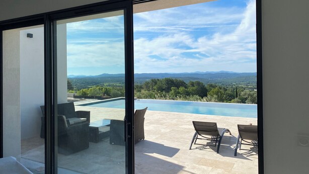 A modern room with a large sliding glass door leading to an outdoor area with a pool and patio furniture. - Beautiful new housse with splendid view and big pool. (Cotignac)