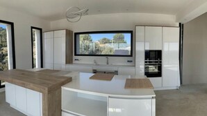 A modern kitchen with a central island, built-in appliances, and a large window offering a view of greenery. - Beautiful new housse with splendid view and big pool. (Cotignac)