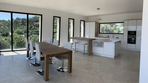 A modern kitchen with a central island, white cabinetry, and large windows offering a view of the outdoors. - Beautiful new housse with splendid view and big pool. (Cotignac)