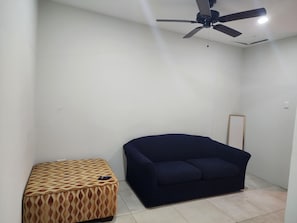 Une pièce dotée d’un ventilateur de plafond, d’un canapé bleu foncé et d’un pouf à motifs.