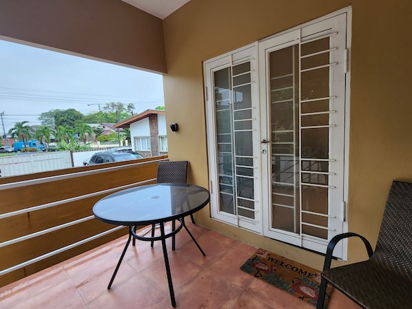 Un balcon avec une table ronde et des chaises, une grande porte vitrée et un paillasson.