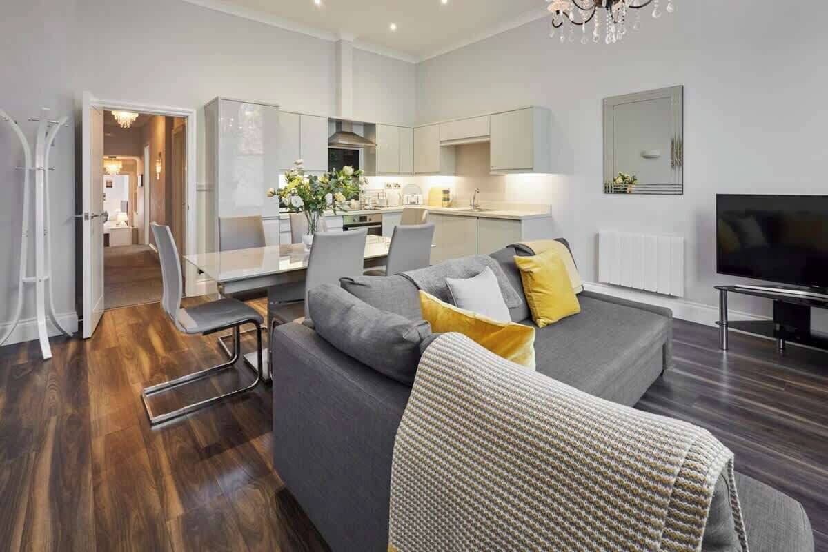 Ein modernes Wohnzimmer mit grauem Sofa, Essbereich und Küche.