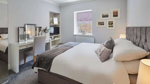 A modern hotel room with a large bed, a desk with a computer, a chair, and a window with a view. - Host & Stay | Brooklands Timeless (Scarborough)