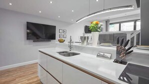 A modern kitchen with a large island, stainless steel sink, and a flat-screen TV mounted on the wall. - Host & Stay | The Old Jail Barber's Shop (Scarborough)