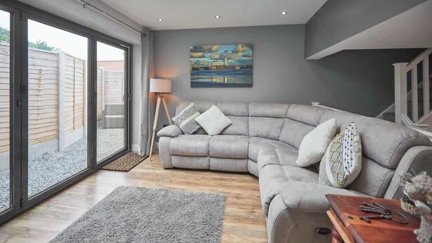 A modern living room with a grey sectional sofa, a wooden coffee table, and a painting on the wall. - Host & Stay | The Old Jail Barber's Shop (Scarborough)