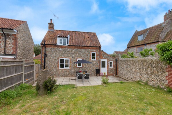 A stone house with a tiled roof, a fenced backyard, and a patio with outdoor furniture.