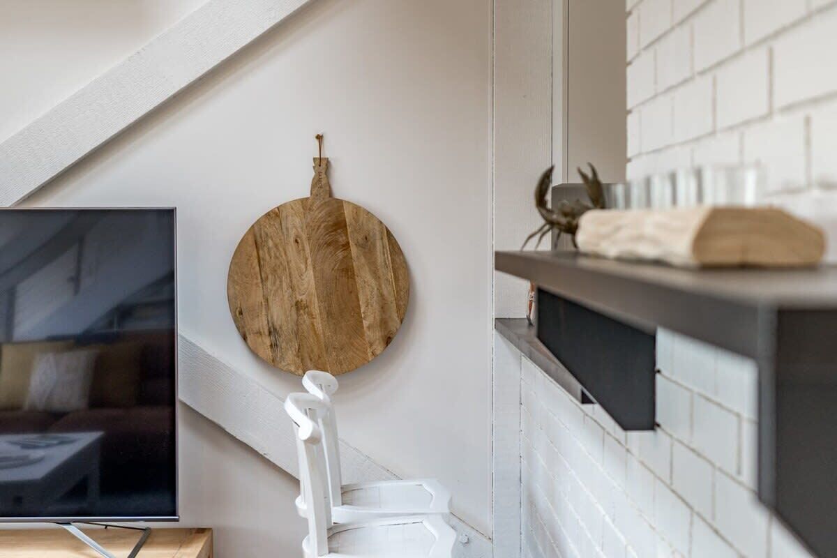 Une salle de bain moderne avec une planche à découper en bois, une chaise blanche, un téléviseur et un mur carrelé.