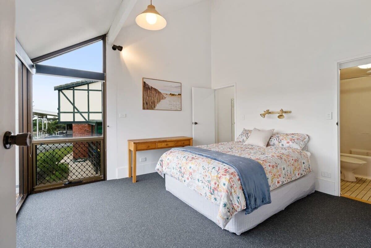 A bedroom with a bed, a desk, a chair, a window, and a door.