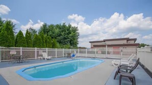 Une piscine entourée d  ’une clôture blanche, avec des chaises longues et un bâtiment en arrière-plan.