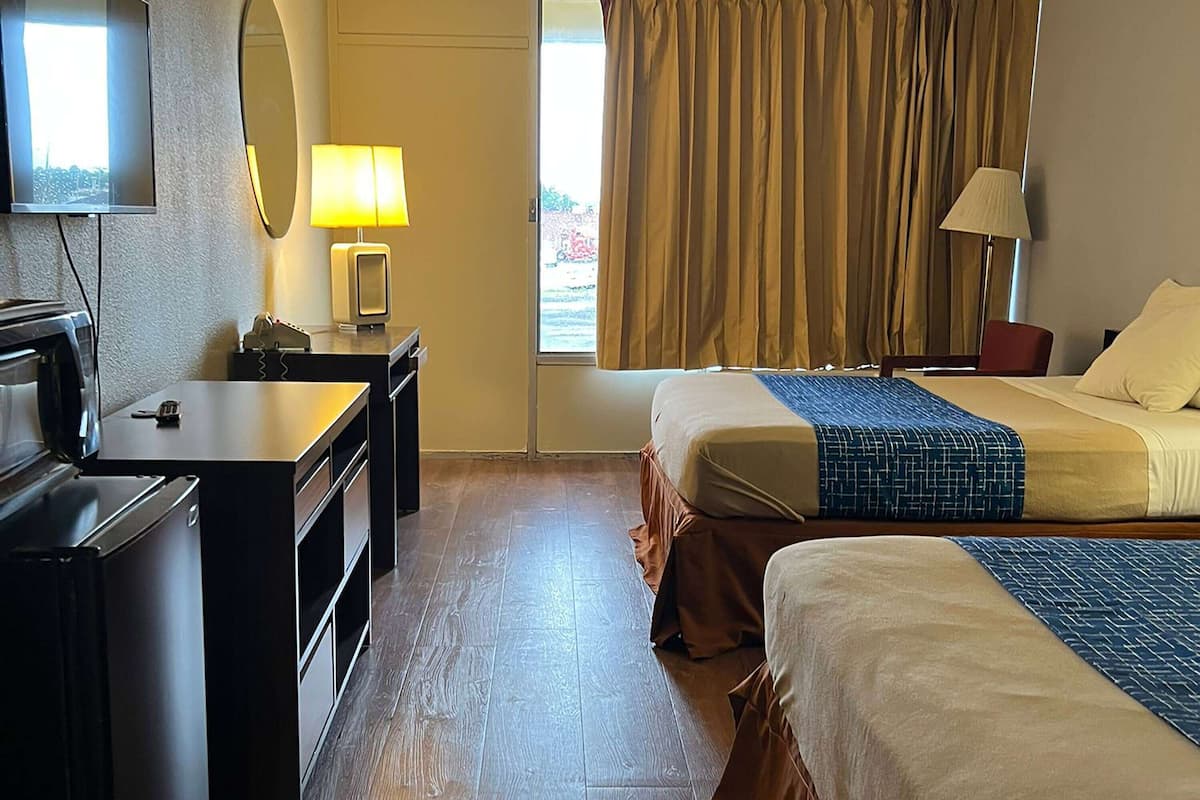 Hotellihuone, jossa on sänky, työpöytä, televisio ja ikkuna, jossa on verhot.