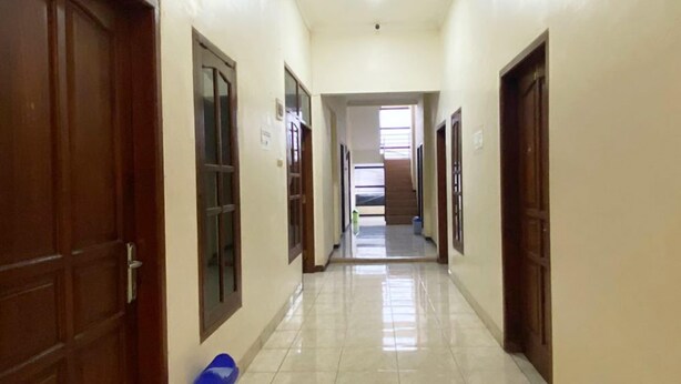 A long, narrow hallway with wooden doors on both sides, leading to a staircase at the end. - Kaja Guest House by Pesen Kamar (Malang)