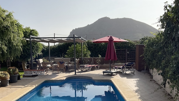 Une piscine entourée de chaises longues et de parasols, agrémentée de plantes en pot et offrant une vue sur une montagne.