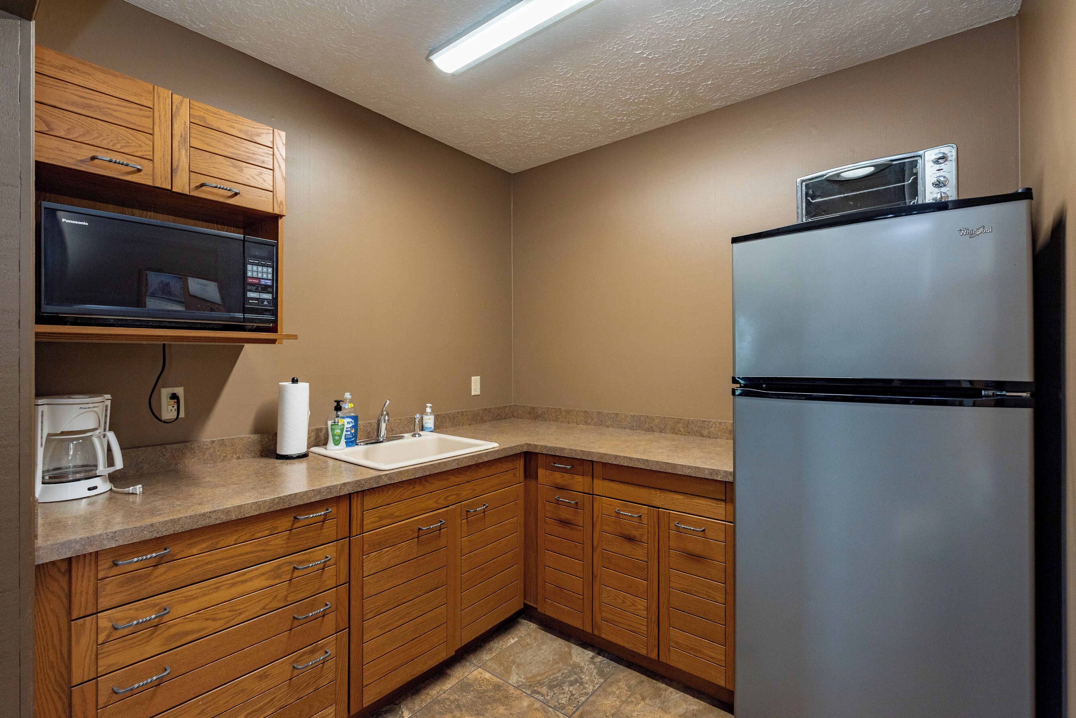 Una cocina con armarios de madera, un refrigerador de acero inoxidable, un microondas, una cafetera y un lavamanos.
