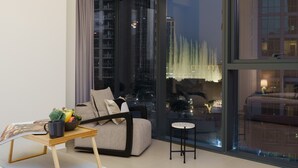 A modern living room with a sofa, a small table with a bowl of fruit, and a view of a cityscape through large windows. - Luxury 2Bedroom w/ Burj Khalifa & Fountain Views (Dubai)
