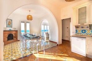 A spacious kitchen with a dining area, a view to the sea, and a tiled floor.