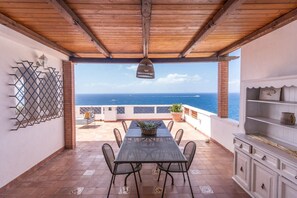 Une terrasse extérieure couverte, avec une table et des chaises, une vue sur la mer et un meuble blanc.