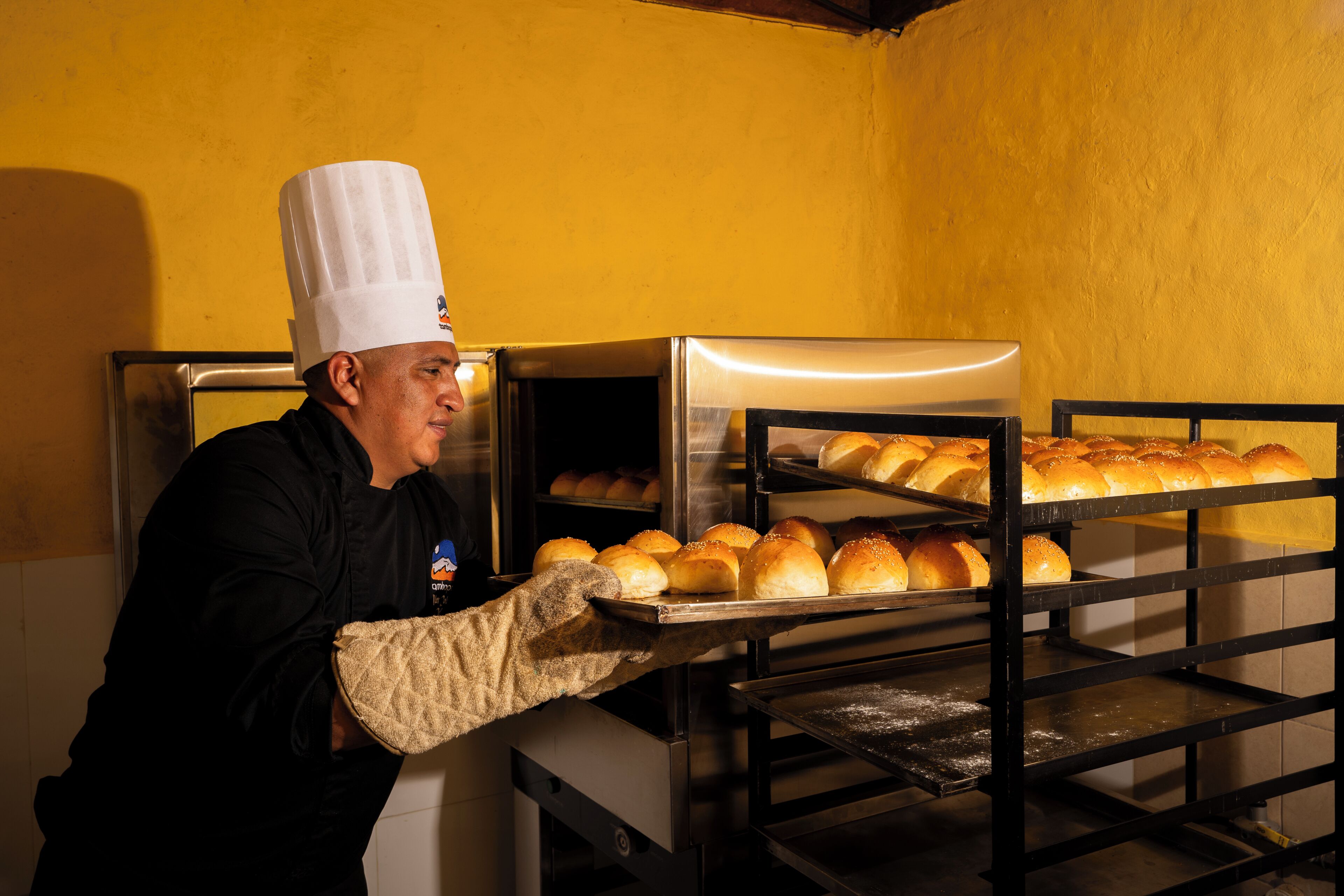 Un chef dans une cuisine professionnelle équipée de fours en acier inoxydable et d’un mur jaune.