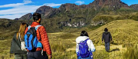 A group of people hiking on a grassy hill with mountains in the background.