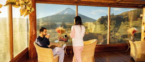 Una habitación con ventanas amplias, muebles de mimbre y vistas a la montaña.
