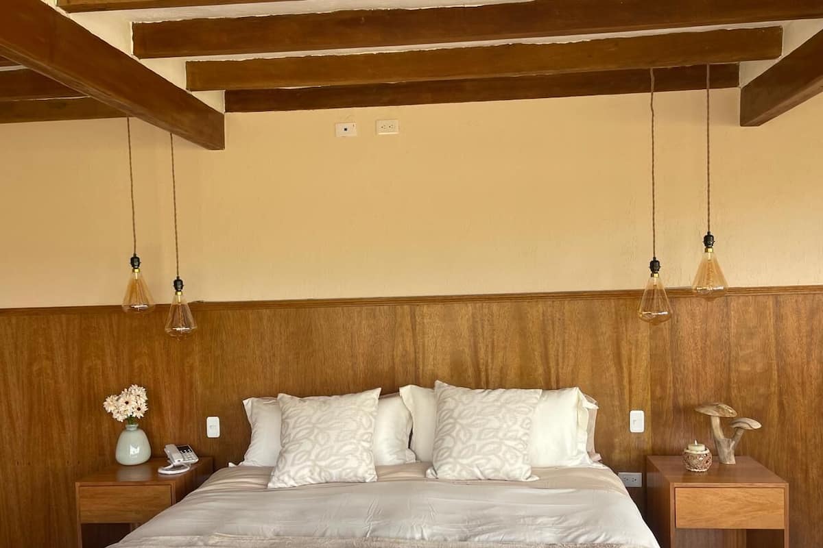 Ein Schlafzimmer mit einem Holz-Kopfteil, einem Bett mit weißer Bettwäsche, zwei Nachttischen mit Lampen und einer Vase mit Blumen auf einem Tisch.