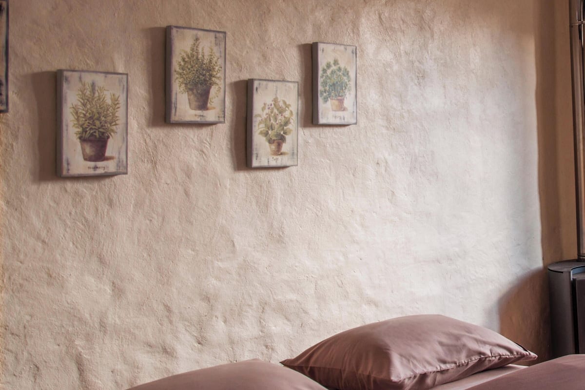 Ein Schlafzimmer mit einem Bett, Kissen und vier gerahmten botanischen Drucken an der Wand.