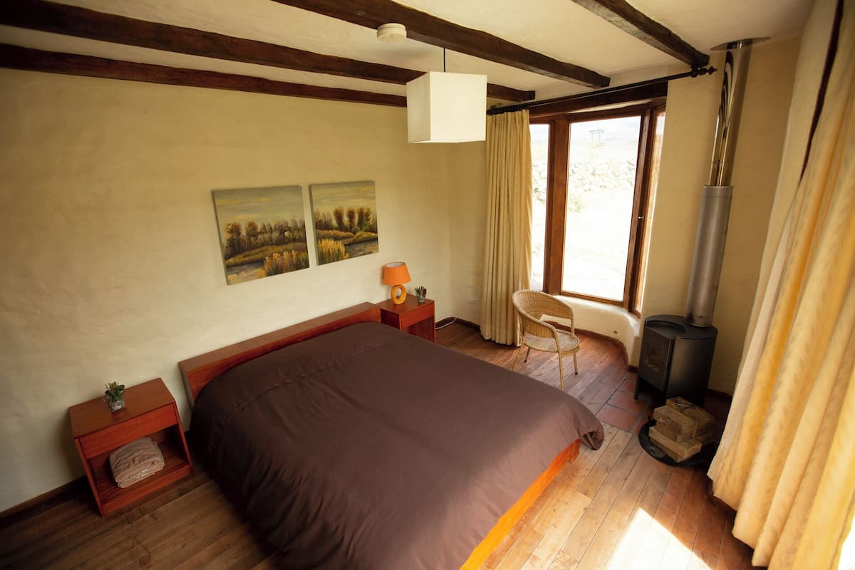 Ein Schlafzimmer mit Bett, Nachttisch, Stuhl, Fenster und Kaminofen.